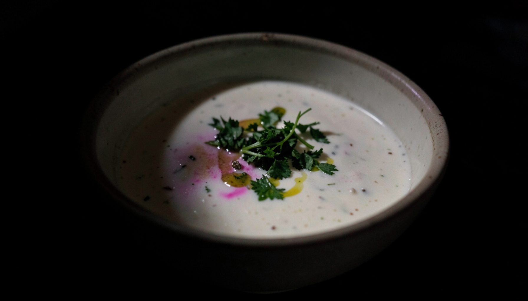 Soupe crémeuse dans un bol en céramique, garnie d'herbes fraîches et d'un filet d'huile, tons verts et blancs