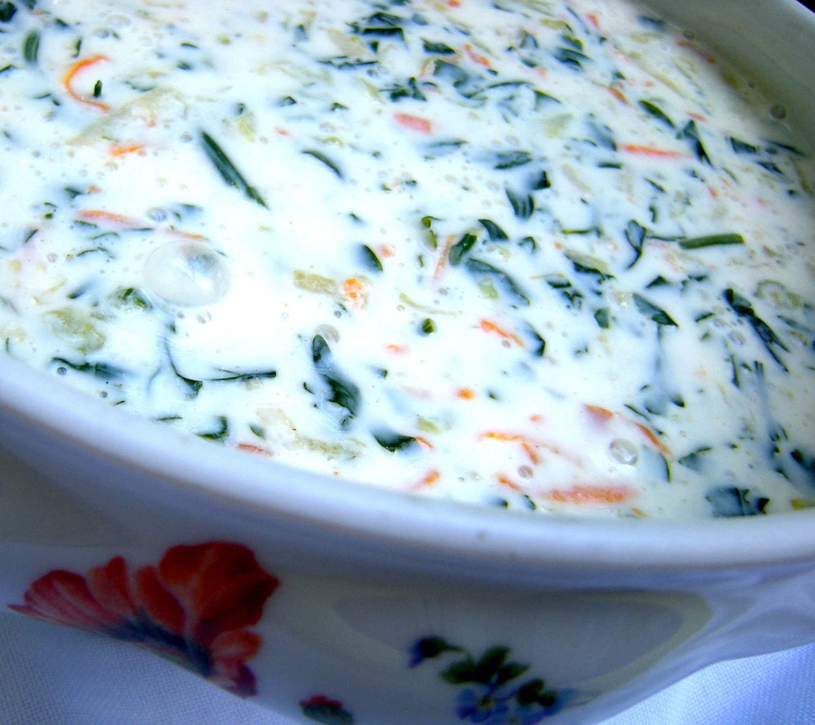 Gros plan d'une soupe blanche crémeuse avec légumes verts et morceaux de carotte, dans un bol à motifs floraux