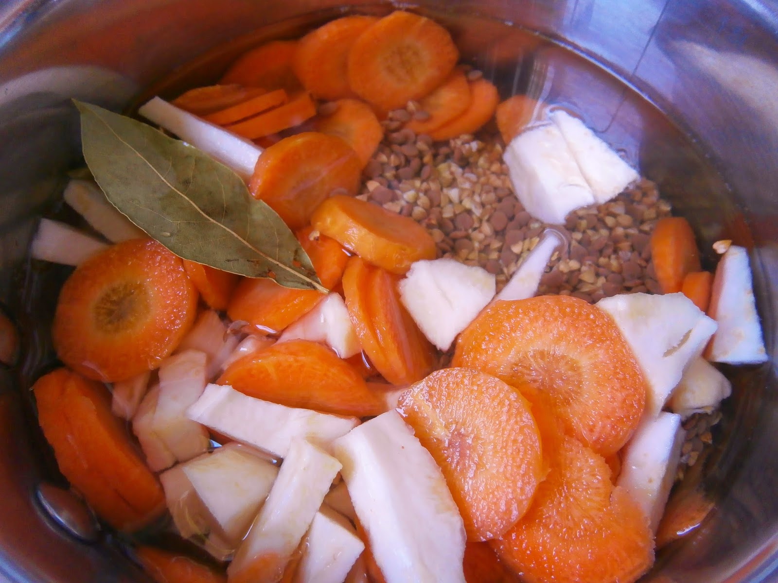 Vue plongeante sur une casserole contenant carottes, panais, sarrasin et feuille de laurier dans l'eau